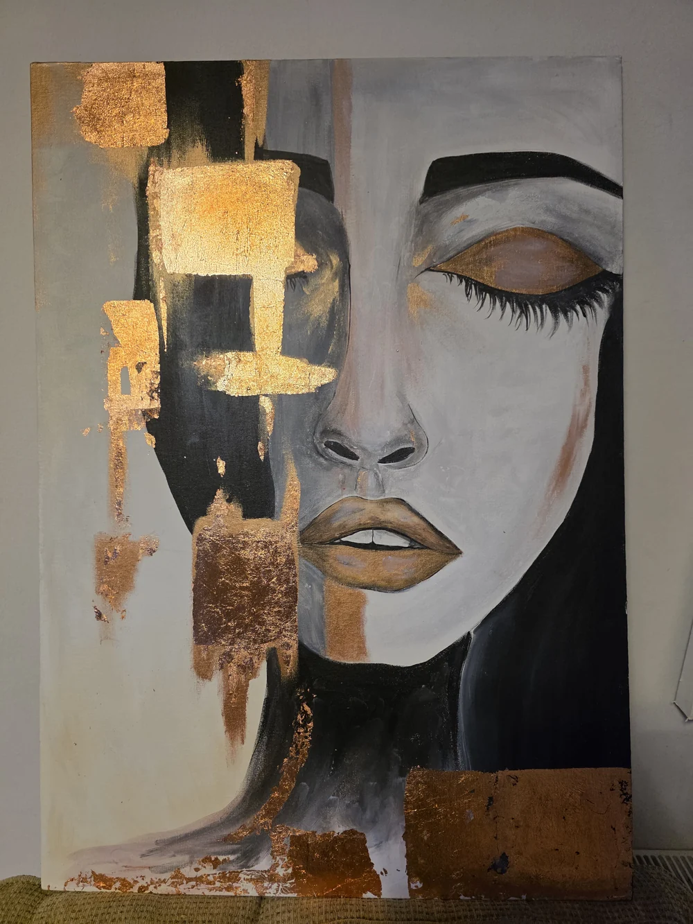 A painted face in pale tones with black and gold textured details.