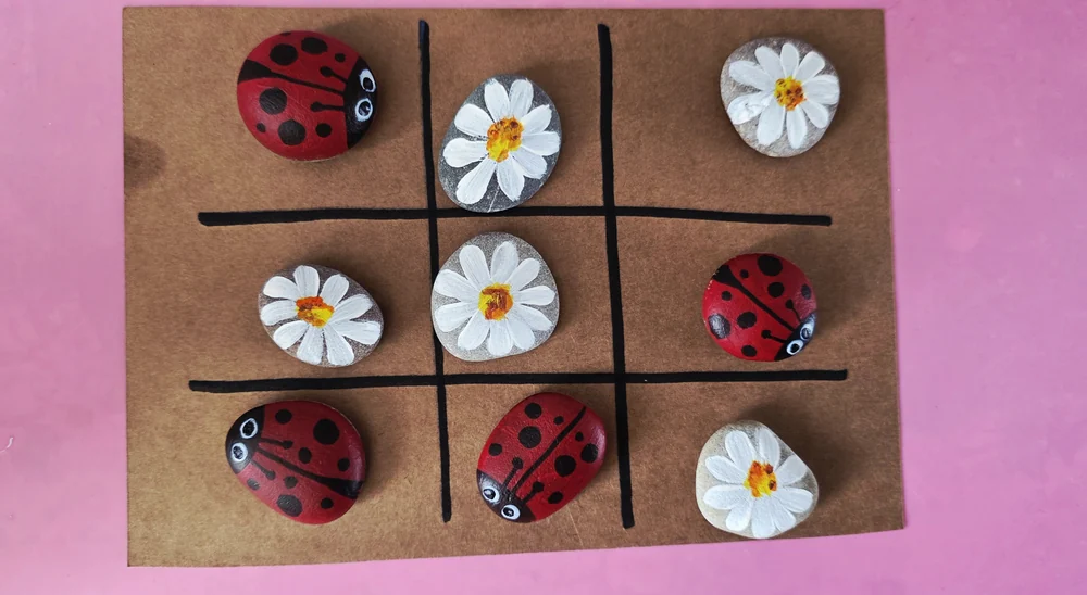 Painted ladybird and daisy counters arranged on a square game board.