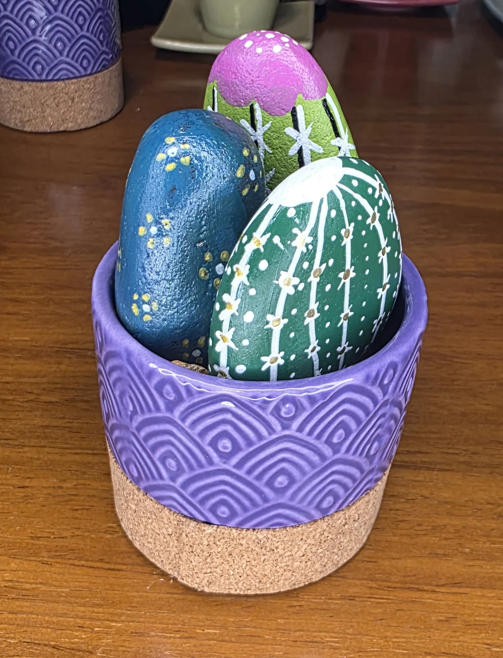 Colourfully painted cactus shapes arranged in a purple patterned pot.