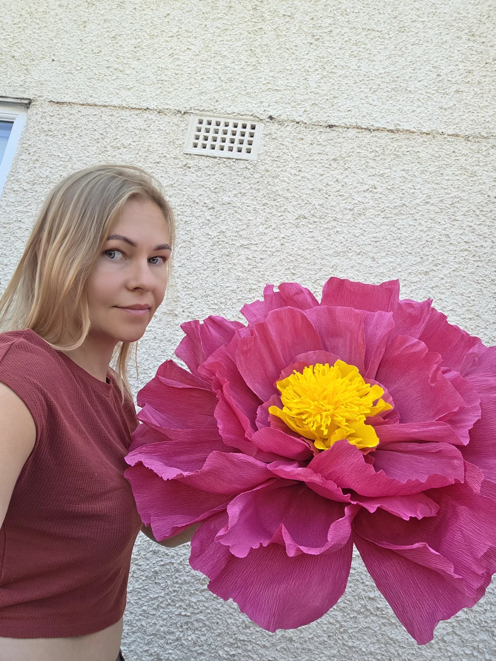 A large handmade pink flower held outdoors.