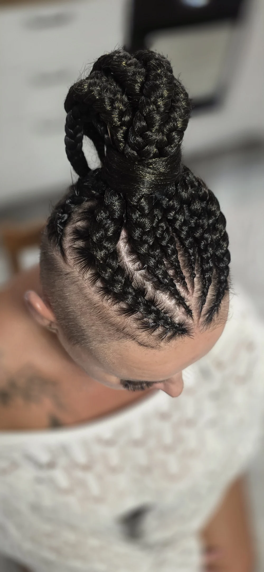 Dark braids gathered into a high bun with patterned partings.