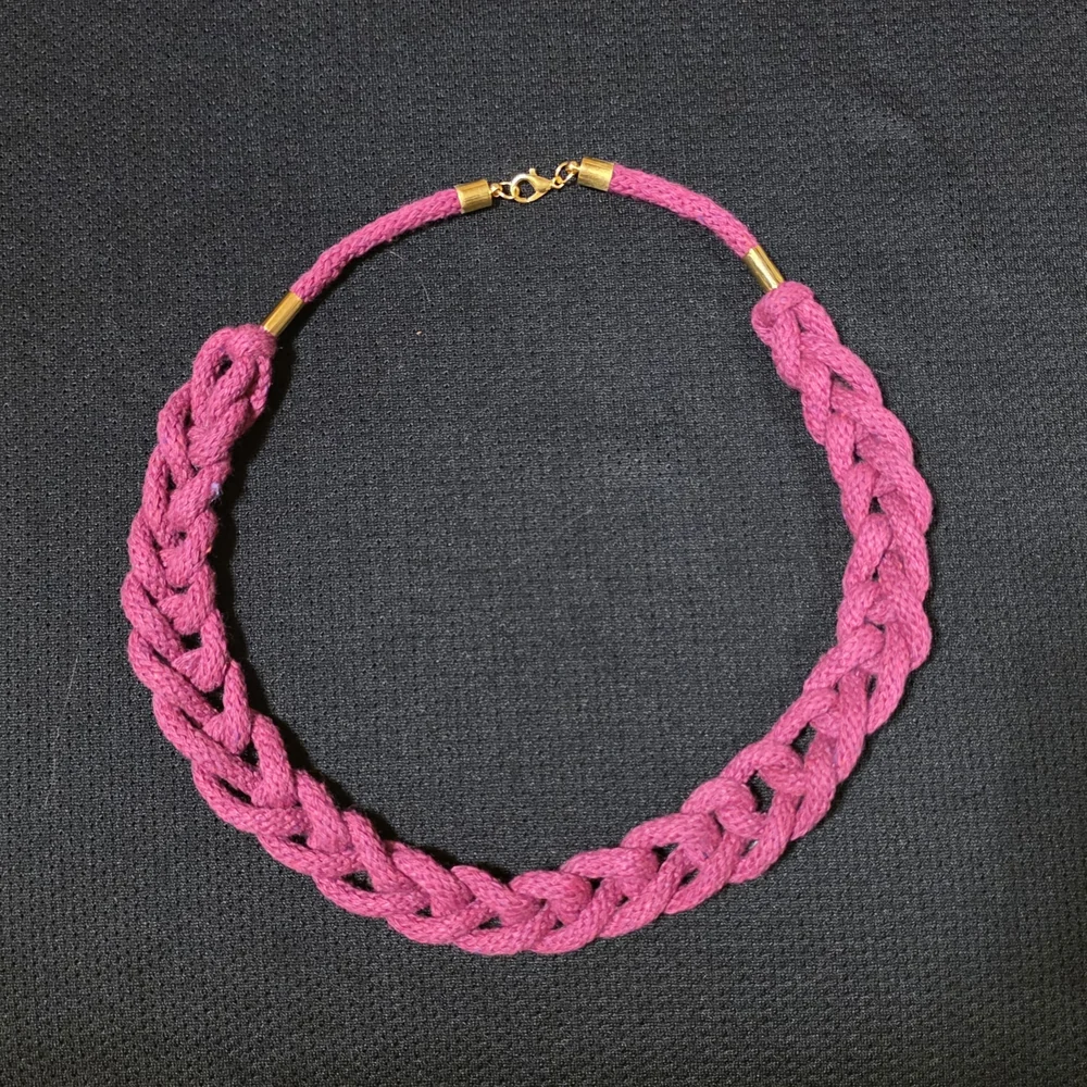 A pink knotted macramé necklace with a gold-coloured clasp.