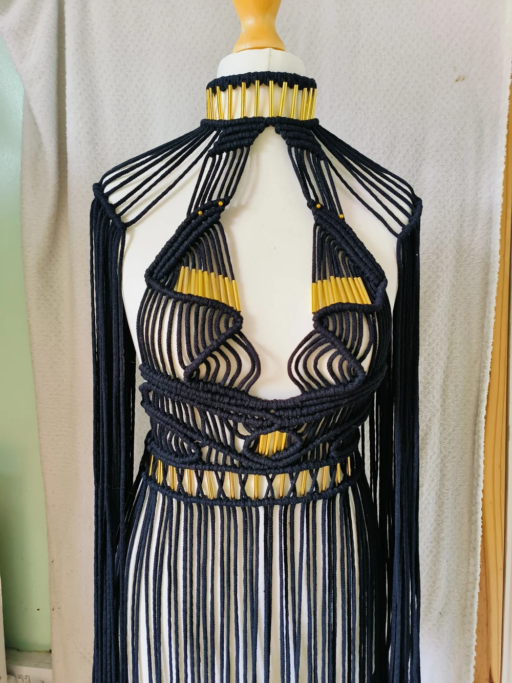 A black knotted macramé garment with long fringe on a dress form.