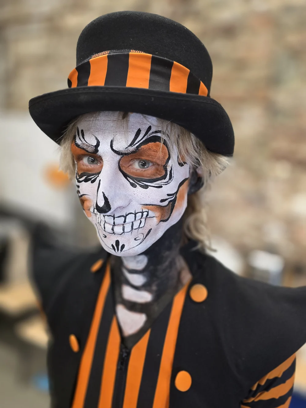 Skeleton face painting with an orange-striped top hat.