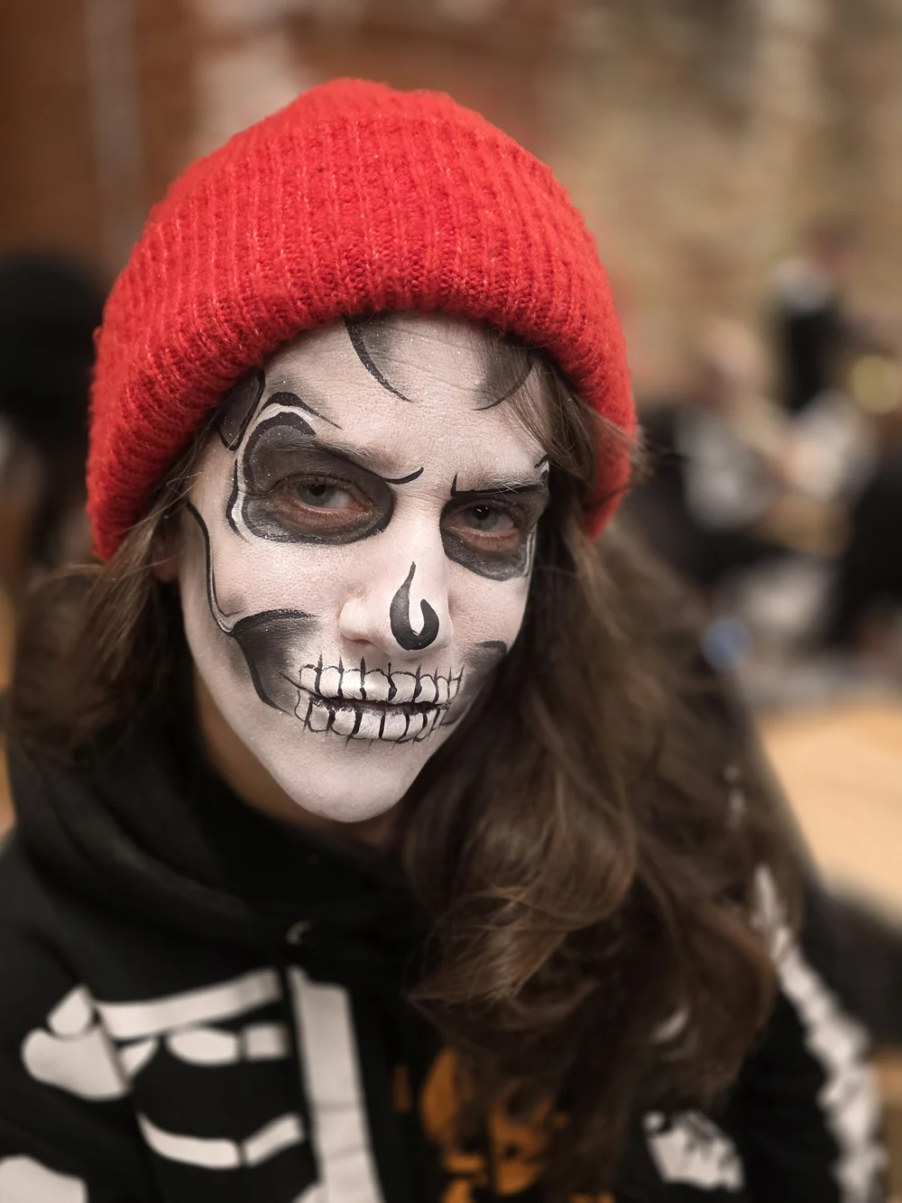 White skull face painting beneath a red knitted hat.