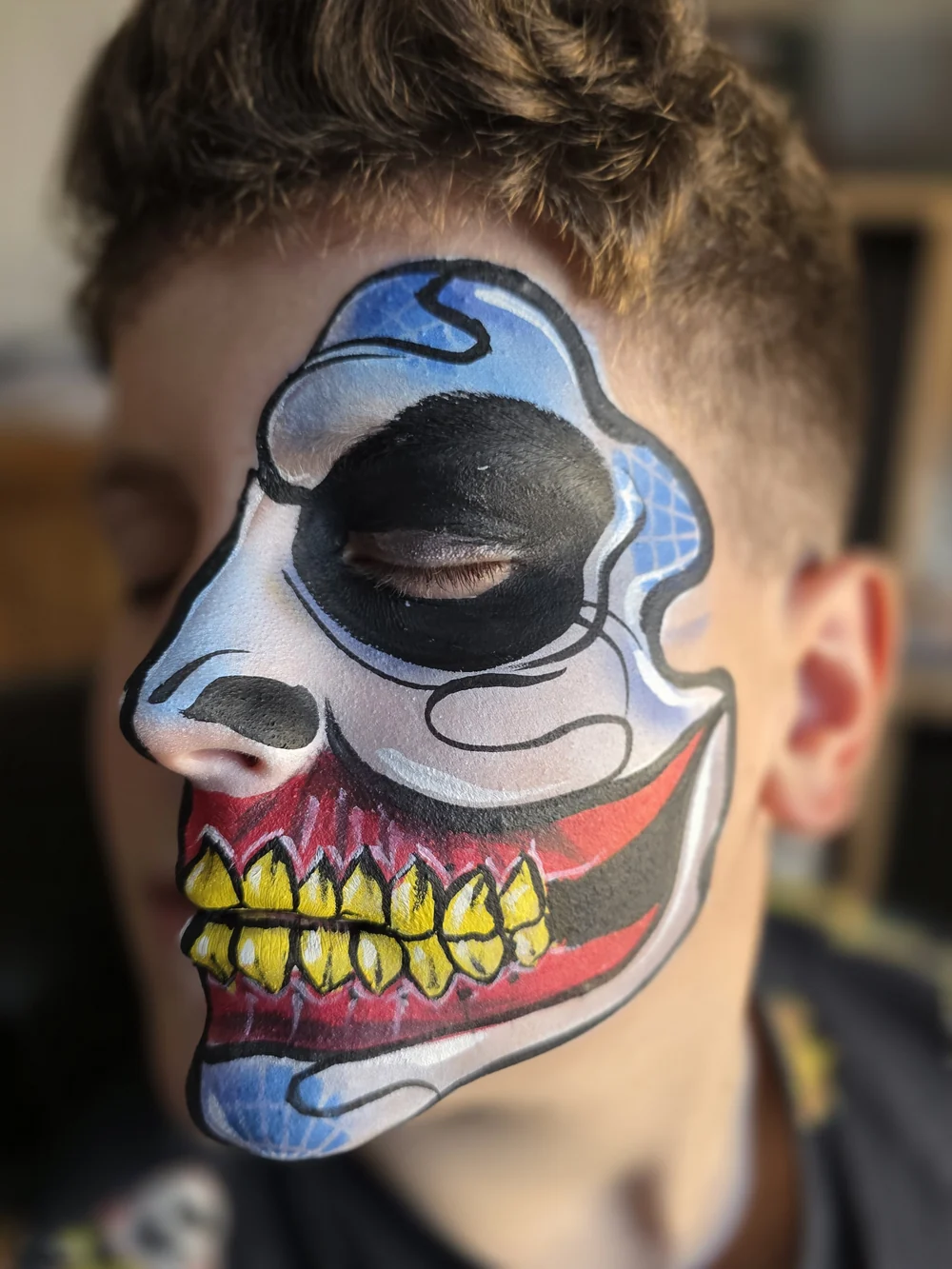 Blue half-skull face painting with a colourful grinning mouth.