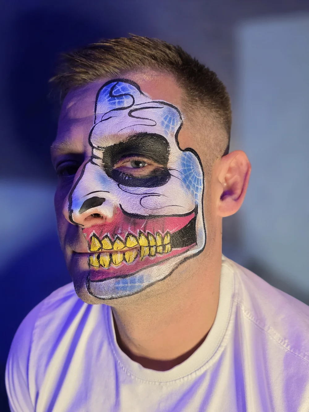 Blue half-skull face painting with purple lighting and rainbow teeth.