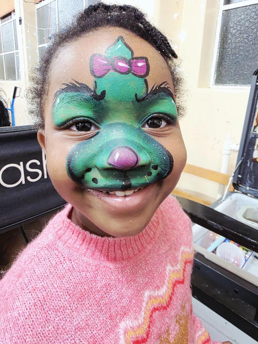 Green cartoon-style face painting with pink decorative details.