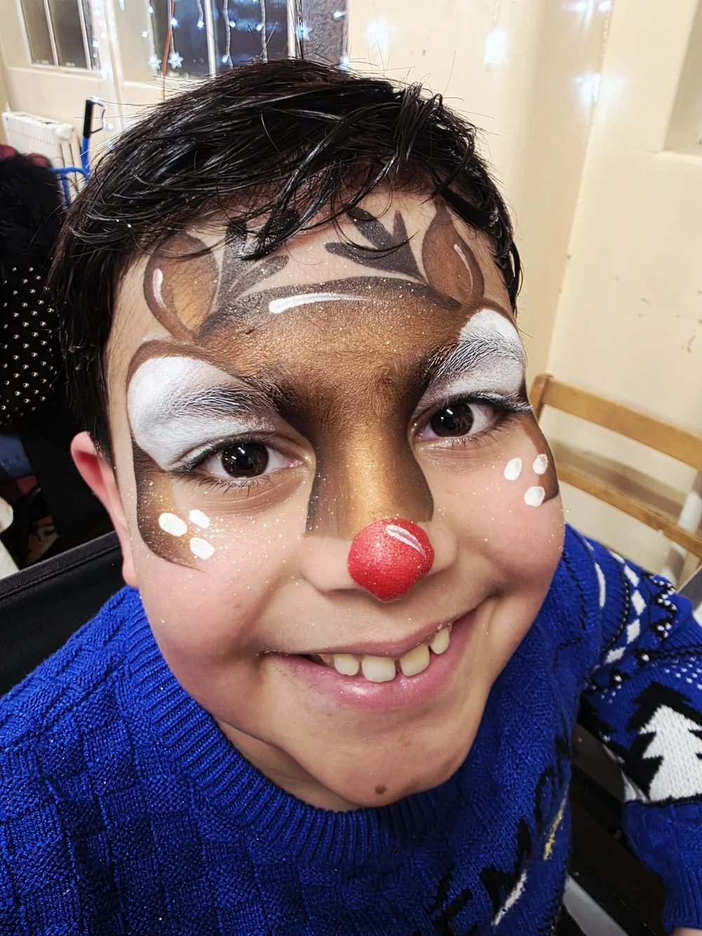 Reindeer face painting with a red nose and white highlights.