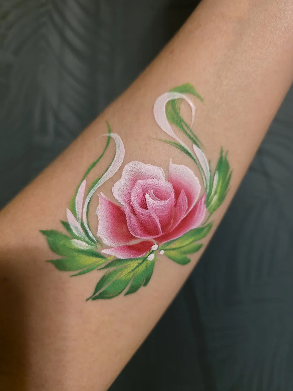 A pink rose with green leaves painted on an arm.