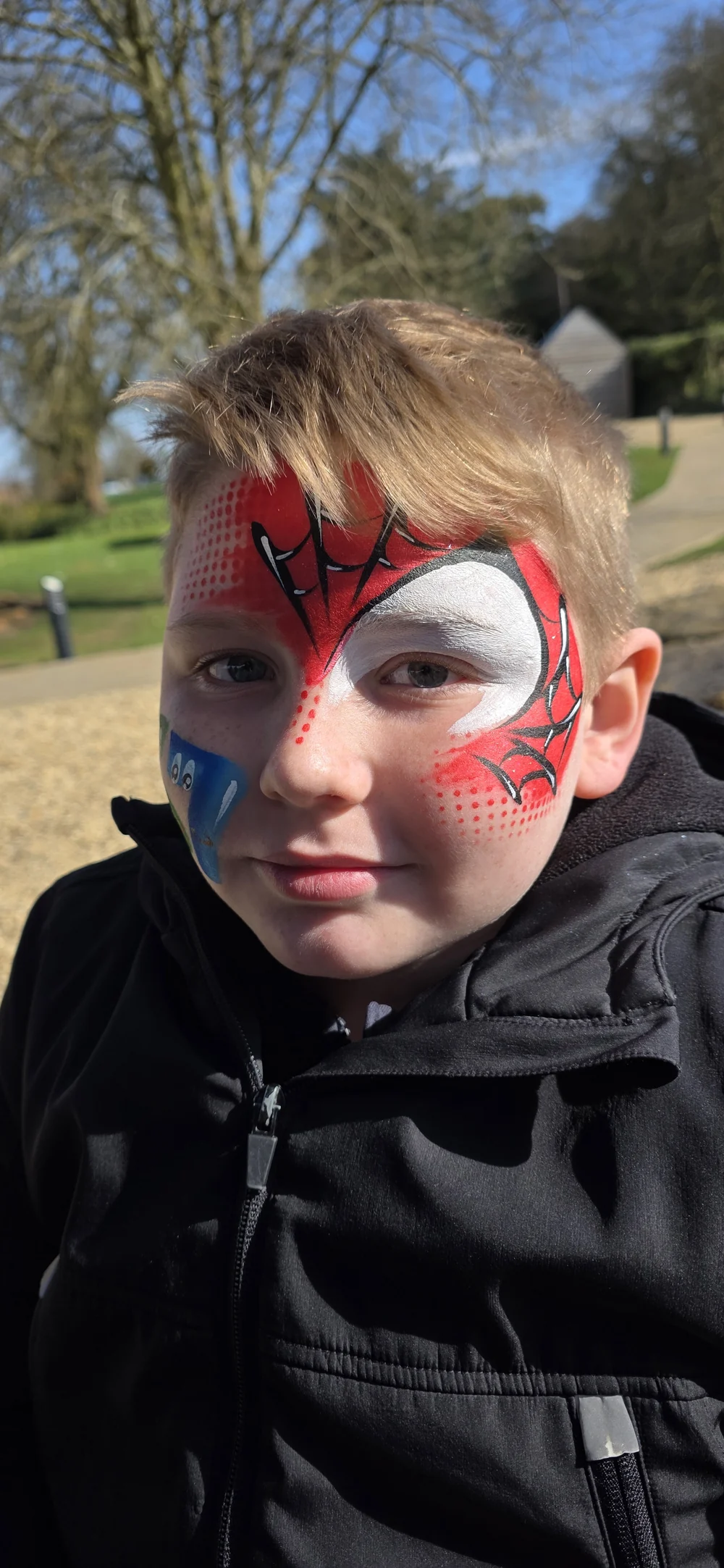 Red and black superhero-style face painting outdoors.
