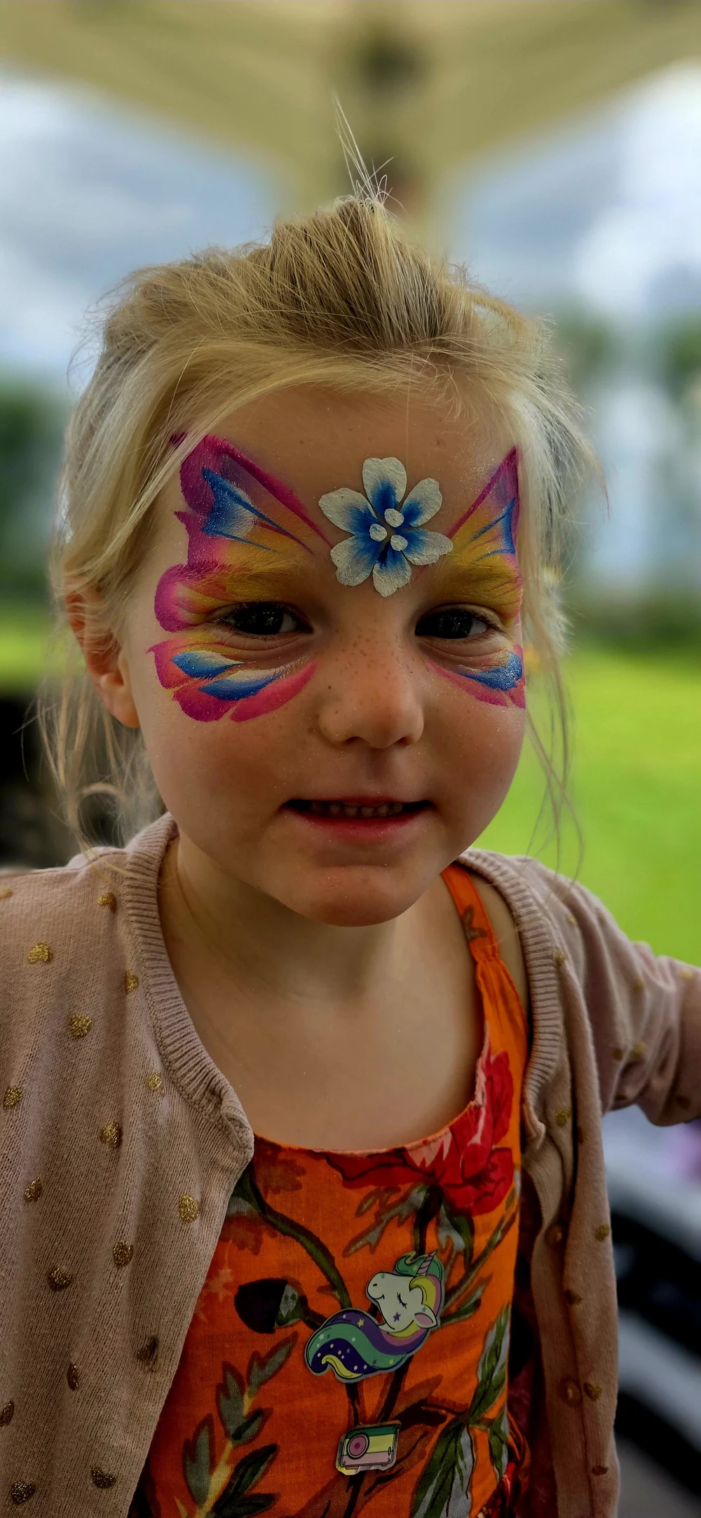 Bright butterfly-style face painting in pink, blue and yellow.
