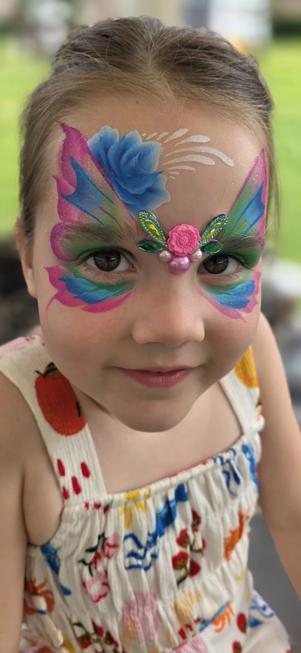 A colourful forehead design with a blue feather motif and pink and green details.