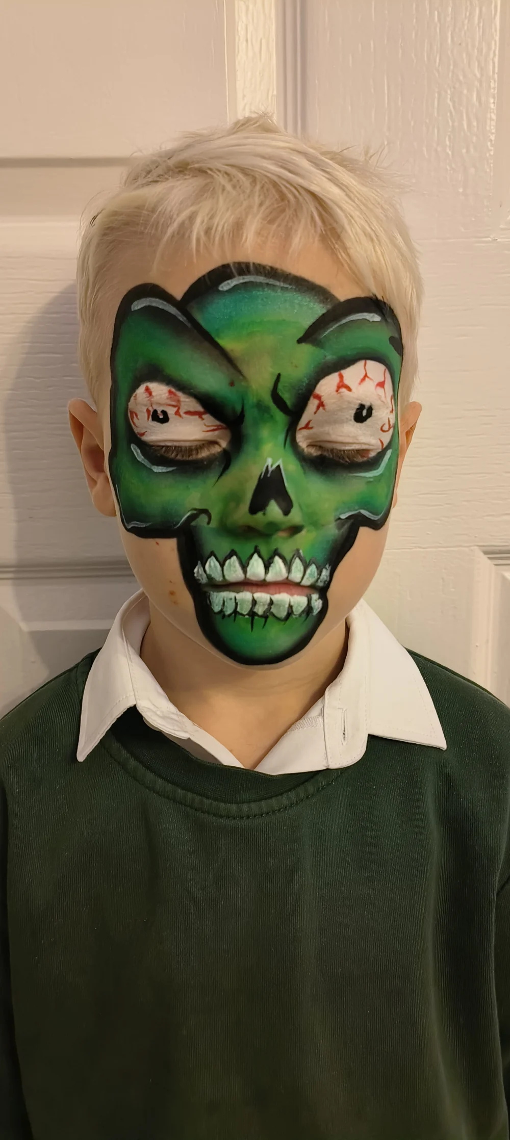 Green monster face painting with dark outlines and sharp teeth.