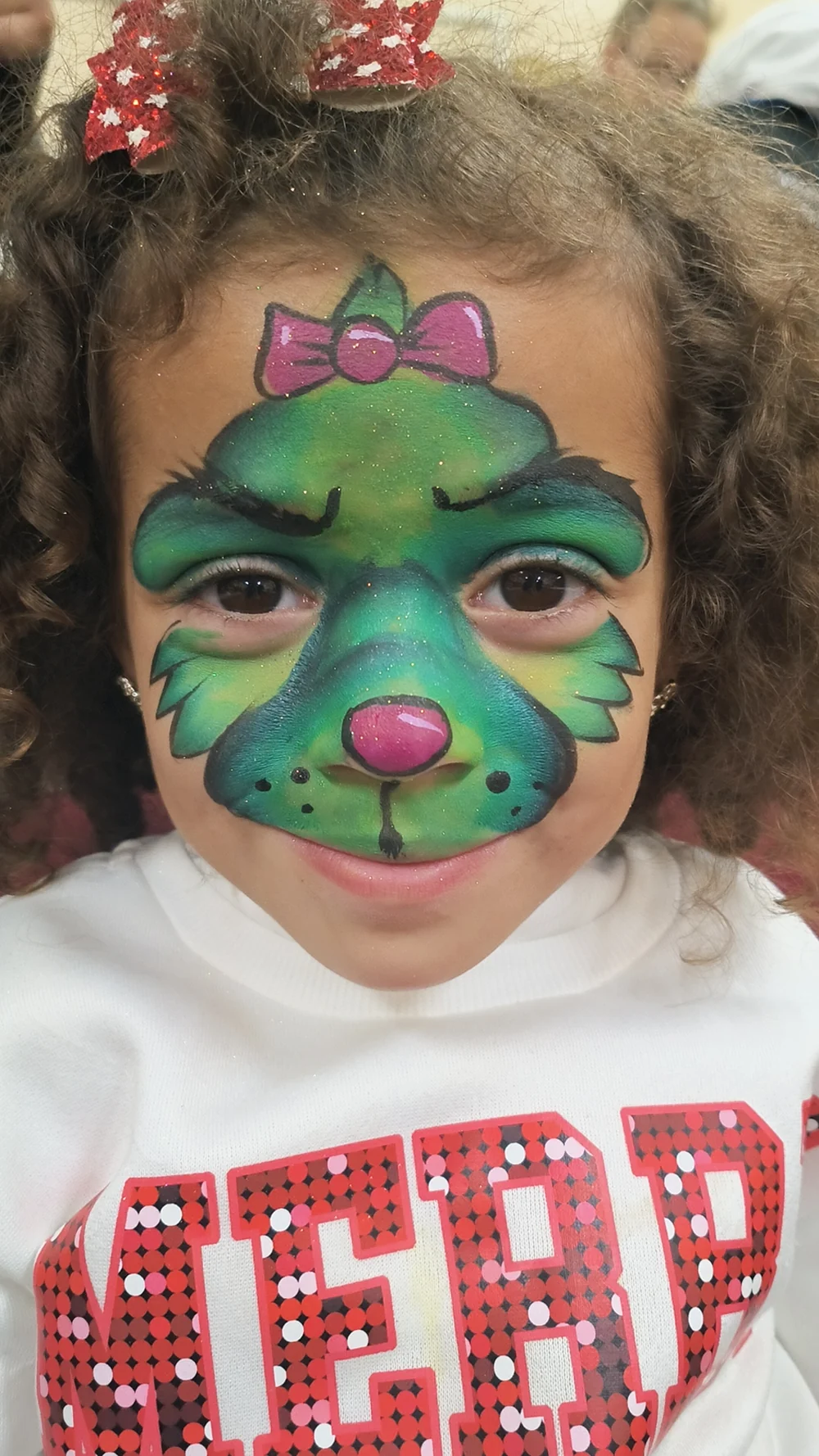 Green cartoon-style face painting with pink and purple accents.