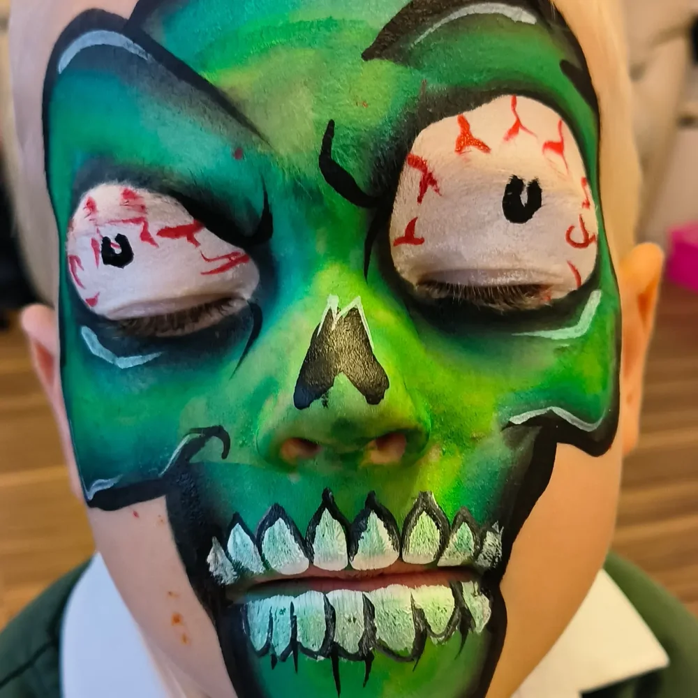 Green skull face painting with a painted eyeball illusion.