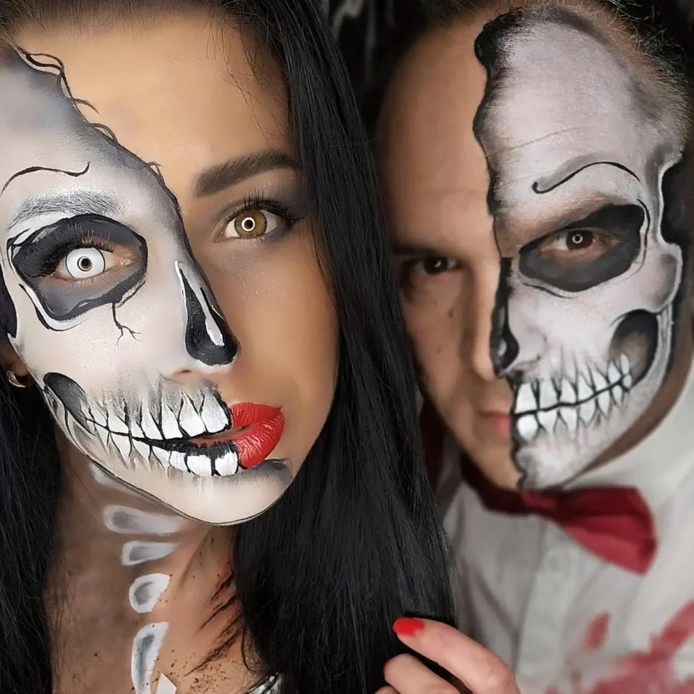 A close portrait of a couple wearing detailed half-skeleton face painting.