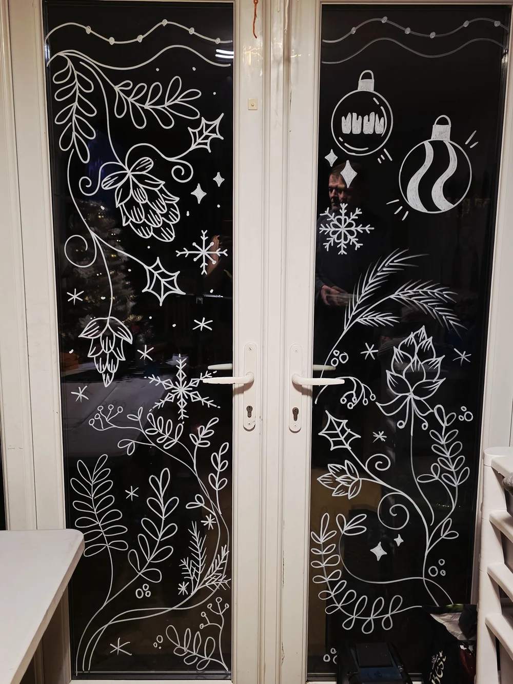 White hand-painted flowers, leaves and stars across dark window panes.