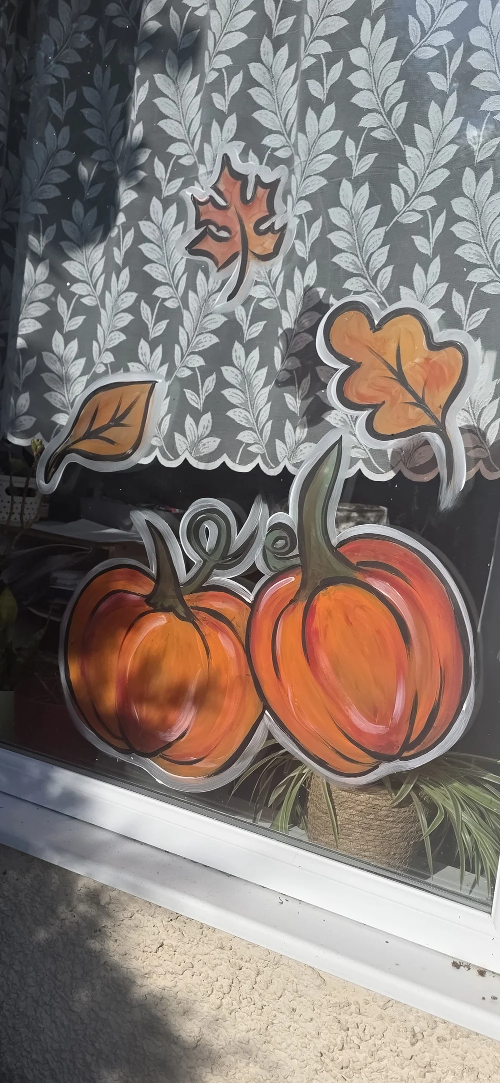 Orange pumpkins and autumn leaves painted on a window.